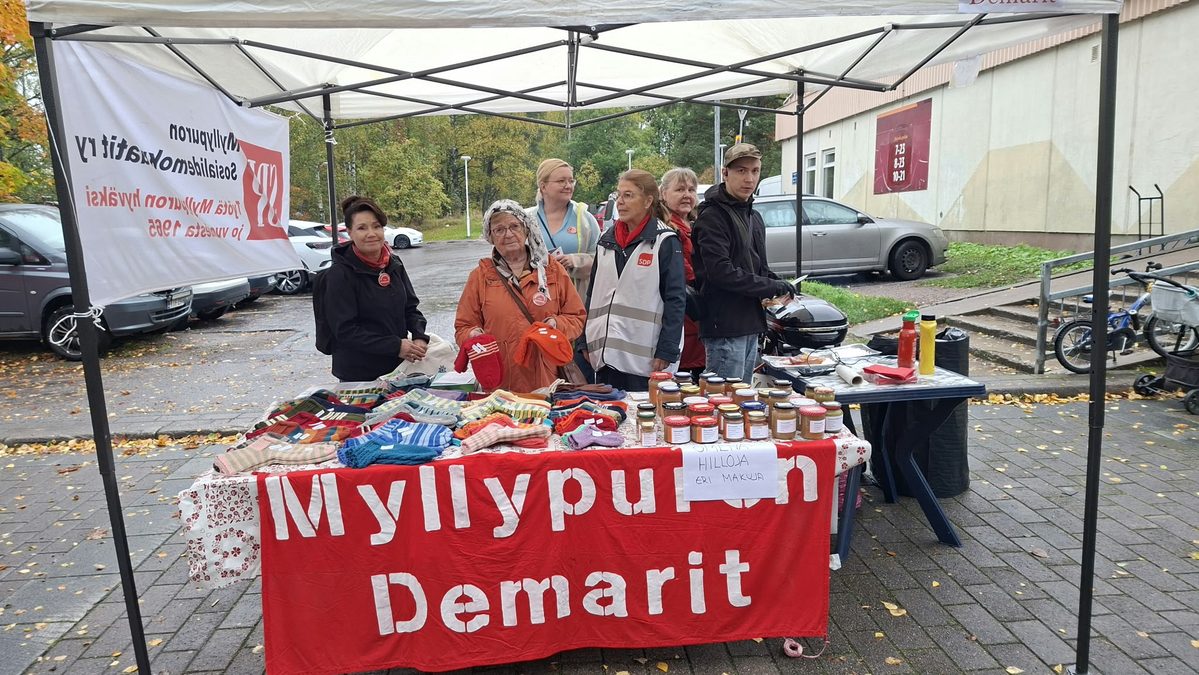 Myllypuron Demarien myyntipöydässä villasukkia ja hillopurkkeja sekä osallistujia teltan alla.